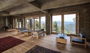 A modern living room with wooden floors, stone walls, and large windows overlooking mountains.