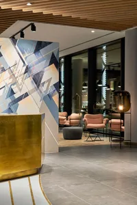 A modern lobby with concrete walls, floor, and ceiling. Features geometric art and pink armchairs.