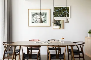 A modern minimalist dining room with a wooden table, black chairs, and concrete pendant lights.