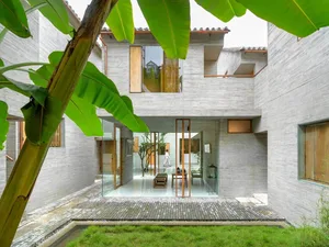 A modern residential house with concrete walls, glass doors, and greenery.