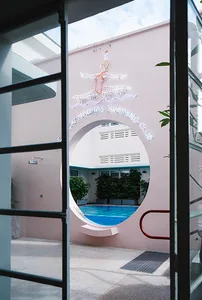 Circular entrance with neon signage for the Madras Swimming Club against a pink wall background.