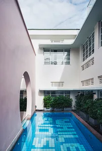 A modern swimming pool surrounded by white walls and greenery.