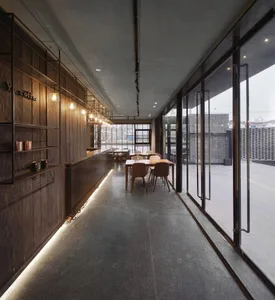 An industrial-themed restaurant interior with concrete walls, wooden furniture, and a long central walkway lined with tables 