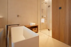 Modern bathroom with concrete walls, a white bathtub, and a glass shower enclosure.