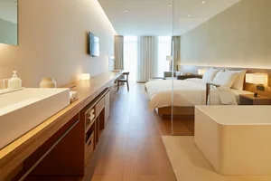 Modern minimalist bedroom with white bed, white walls, and white materials.