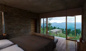 A modern bedroom with wooden walls, a bed, and a view of mountains and trees.