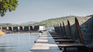 Minimalist floating saunas and water huts on a calm water body with a wooden dock leading to them.