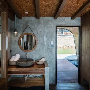 An industrial-style bathroom features a concrete sink and mirror, with a view of the water.