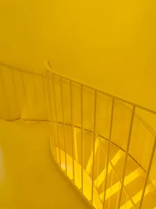 A minimalist staircase with a yellow metal railing and walls.