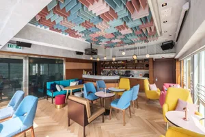A stylish modern bar interior featuring colorful seating and a well-stocked bar counter.