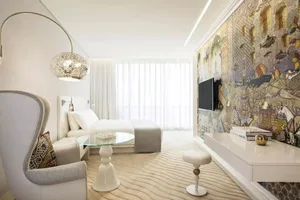Modern bedroom featuring a bed with white linens, a white armchair with decorative accents, a glass coffee table, and a decor