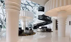 Modern hotel lobby featuring white marble flooring, black metal spiral staircase, and contemporary seating.