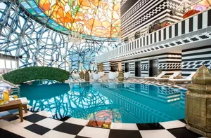 Modern hotel pool deck featuring glass and metal structural elements and a vibrant stained glass ceiling design.