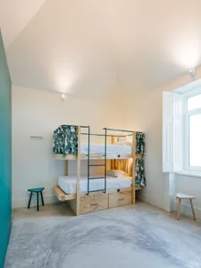 A minimalist bedroom featuring a wooden bunk bed with a ladder and storage drawers below, modern lighting, and a concrete flo