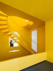 A modern, brightly colored yellow spiral staircase with a person and child looking up.