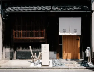 A modern Japanese cafe exterior with a kitchen table in front of it, featuring wooden elements, stone ground, and ceramic dec