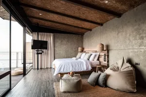 Modern industrial bedroom featuring wooden elements and a concrete wall, with a large bed and a flat-screen television.