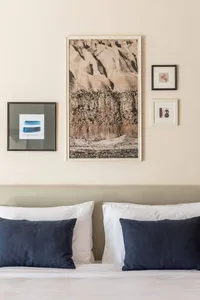 A minimalist bedroom with a framed print of a textured wall on the wall above the bed, complemented by dark blue cushions and