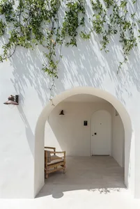 Archway under white wall with vines hanging down and a rattan chair.