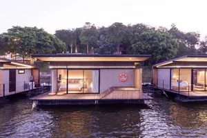 Modern minimalist floating house with a wooden deck, glass walls, and concrete roof.