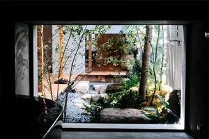 A serene minimalist garden interior with natural stone, plants, and a wooden deck.