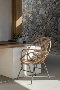 A minimalist interior design featuring a rattan chair, a stone wall, and a wooden table.