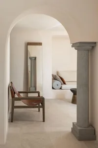A minimalist living room with concrete walls, a brown leather chair, and a sofa with pillows.