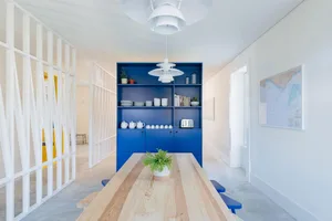 A minimalist living room and kitchen featuring wooden and concrete surfaces, canvas walls, and blue accents.