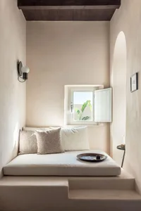 A minimalist living space with light-colored concrete and covered seating area with cushions and pillows.