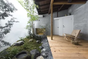 A minimalist verandah interior with wooden flooring, concrete walls, and plants.