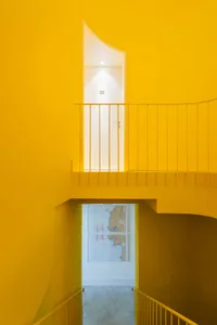 A minimalist staircase with bright yellow walls and a metal railing leading to a white door.
