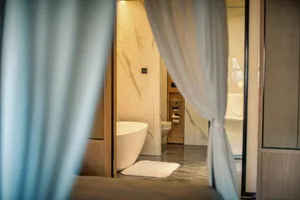 A modern bathroom featuring white marble walls and flooring, a freestanding bathtub, and a toilet with a white towel.