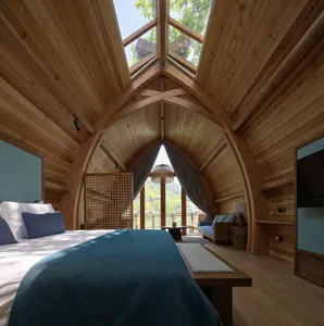 A spacious bedroom with a vaulted wooden ceiling, large glass windows, and a comfortable bed adorned with blue textiles.