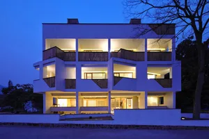 Modern apartment building with concrete and wood materials, illuminated at dusk