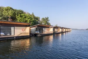 現代浮動房屋擁有木質外牆、混凝土基座與帆布屋頂，坐落於平靜水面上。