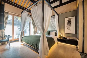 A modern minimalist bedroom featuring a canopy bed with white curtains, wooden flooring, and a black and white abstract paint