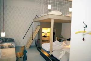 A modern minimalist bedroom with a wooden platform bed, white linens, and a hanging light fixture.