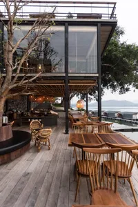 Outdoor restaurant deck featuring modern architecture, wood and bamboo materials, and a view of a lake.