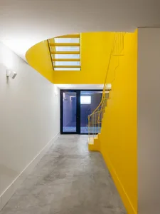 A minimalist interior design featuring a modern staircase with yellow metal railing and handrail, set against a white backgro