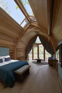 A stylish, wooden bedroom with arched ceiling, large windows, and a comfortable bed.