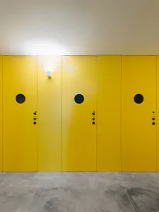 A row of bright yellow doors with dark circular holes and small black handles and locks, mounted on a concrete wall.
