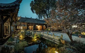 傳統中式住宅外觀，石牆、木門，以及夜色中橫跨池塘的石橋。