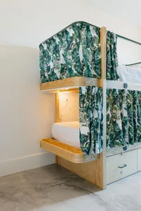 A modern, industrial-style bedroom with a wooden platform bed featuring tropical-themed curtains and a built-in drawer unit.