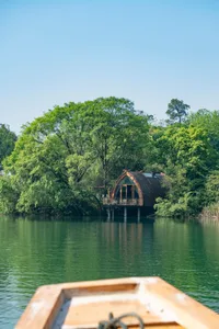 A wooden cabin on stilts surrounded by green trees and a calm lake.