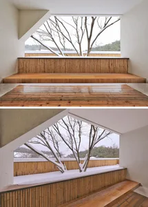A modern architectural staircase with wooden steps and a wooden railing, featuring a view of a snowy tree.