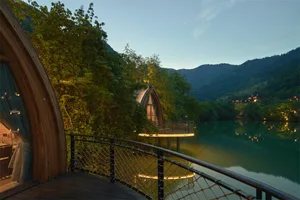 Hotel room with arched window overlooking tranquil water and mountains at dusk, built on stilts over calm lake.