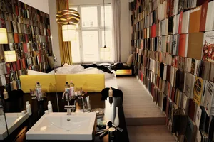 A minimalist bedroom filled with books on the walls and a bed with a bright yellow headboard.