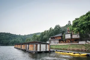 Modern floating huts aligned along a lake with a large building in the background.