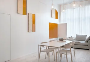 A modern, minimalist living room with a white table and chairs, light wooden flooring, white curtains, and orange accent piec