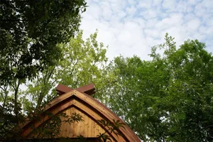 A wooden church roof featuring a wooden cross against a backdrop of green trees and a blue sky.